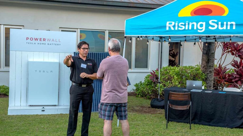 man standing in front of tesla powerwall and solar panel explaining how they work
